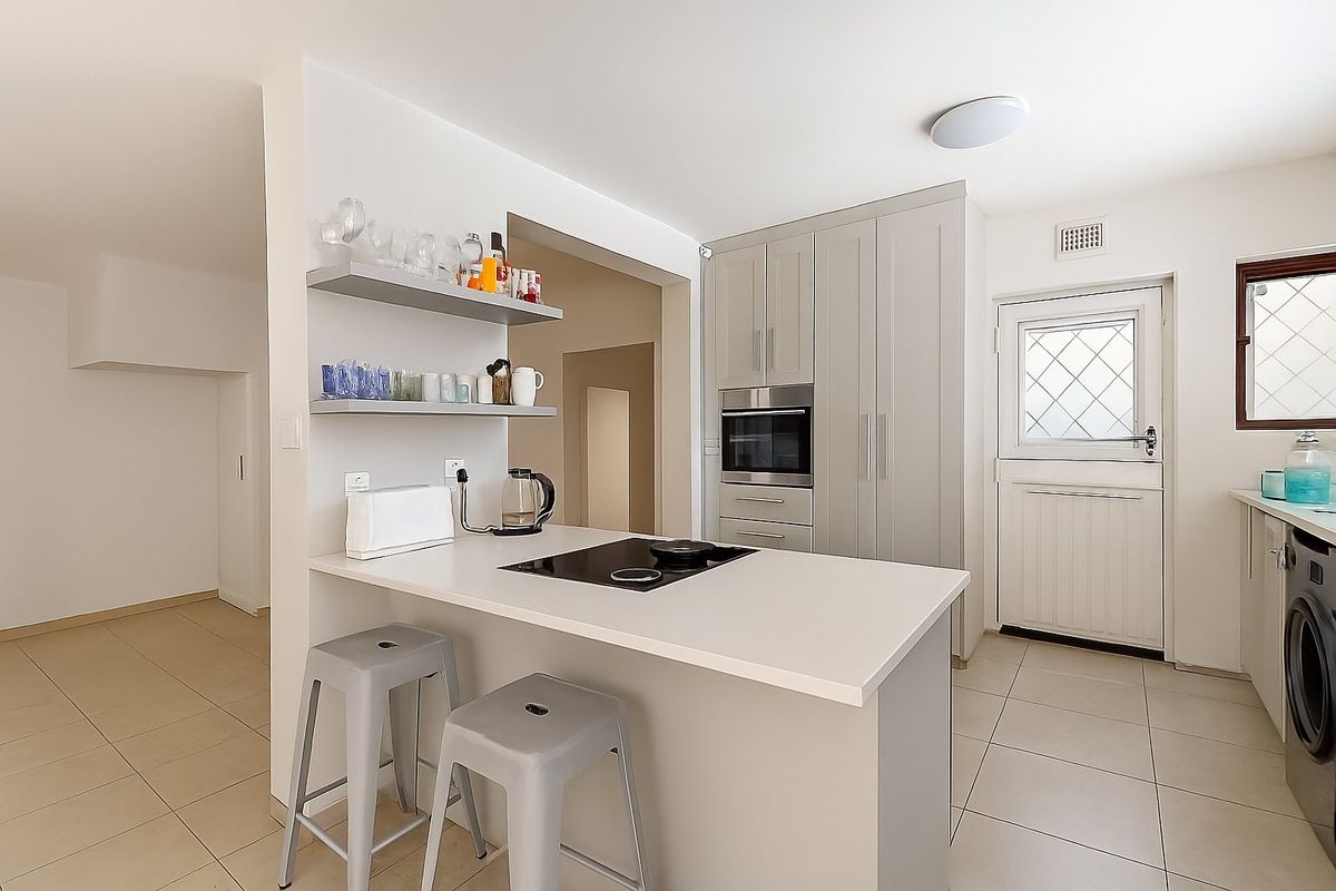 Modern kitchen featuring light grey cabinetry, a built-in oven, electric hob, and tiled flooring, with a convenient breakfast bar and direct exterior access.