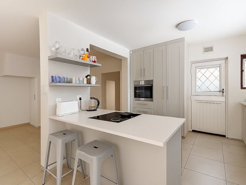 Modern kitchen featuring light grey cabinetry, a built-in oven, electric hob, and tiled flooring, with a convenient breakfast bar and direct exterior access.