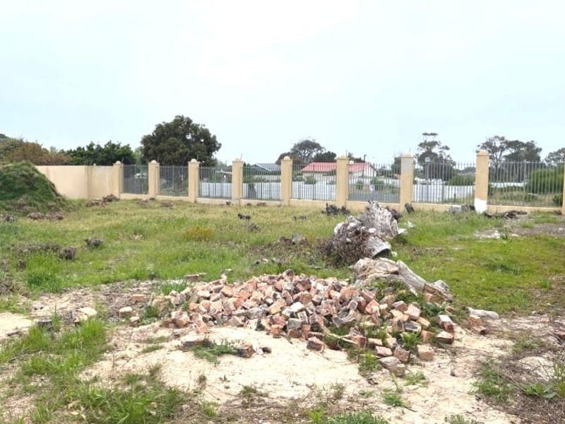 A vacant residential plot featuring a perimeter wall and metal fencing, currently containing scattered debris and overgrown vegetation.