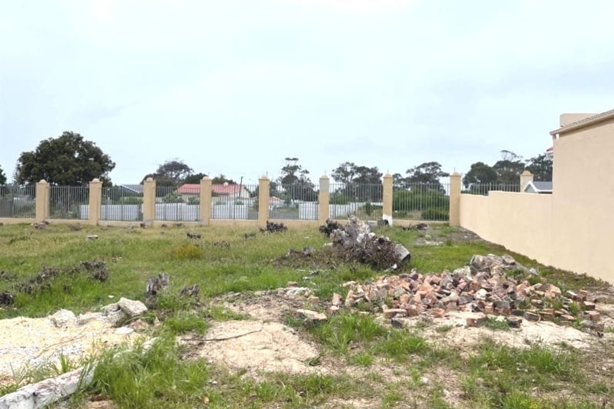 A vacant residential plot featuring a perimeter wall with metal fencing and concrete pillars, currently containing debris and tree stumps.