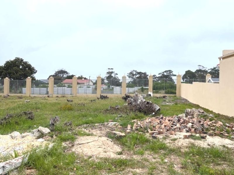 A vacant residential plot featuring a perimeter wall with metal fencing and concrete pillars, currently containing debris and tree stumps.