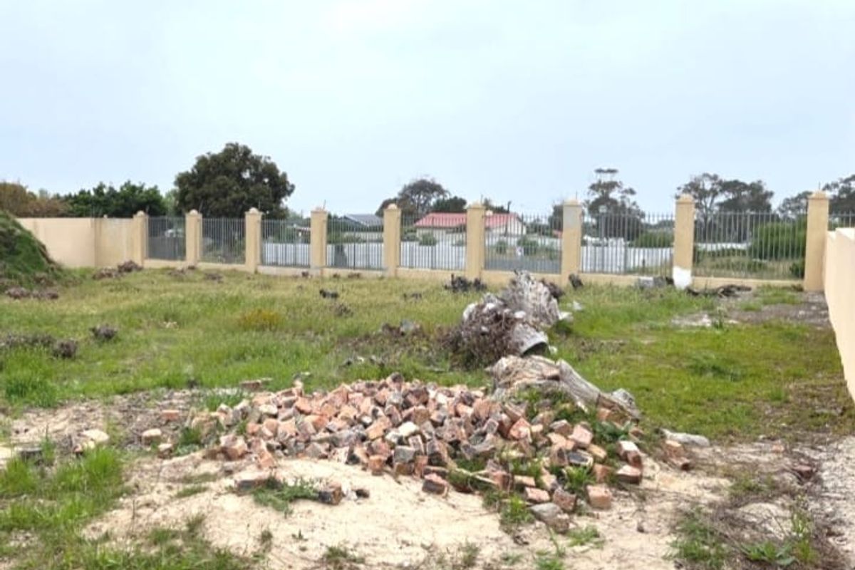 A vacant residential plot featuring a perimeter wall with metal fencing, currently containing scattered debris and natural vegetation.