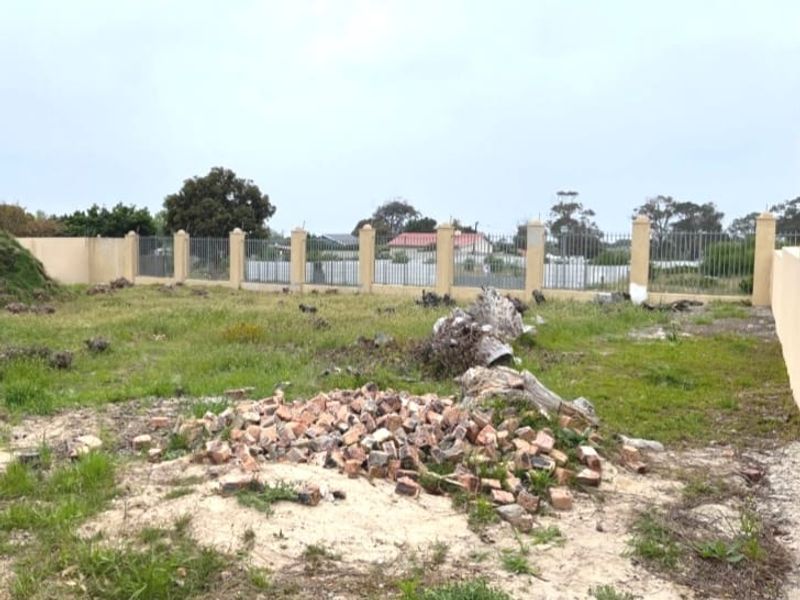 A vacant residential plot featuring a perimeter wall with metal fencing, currently containing scattered debris and natural vegetation.