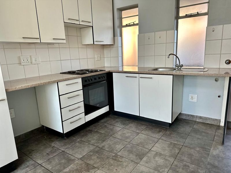 A functional kitchen featuring white cabinetry, a built-in oven with electric hob, tiled backsplash, and a stainless steel sink.