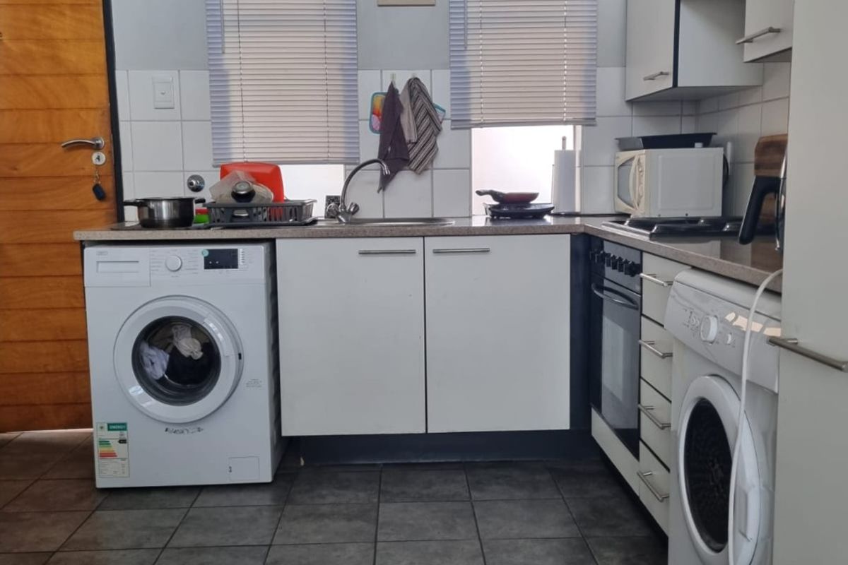 Functional kitchen featuring white cabinetry, tiled backsplash, built-in oven, and integrated laundry appliances with dark floor tiling.