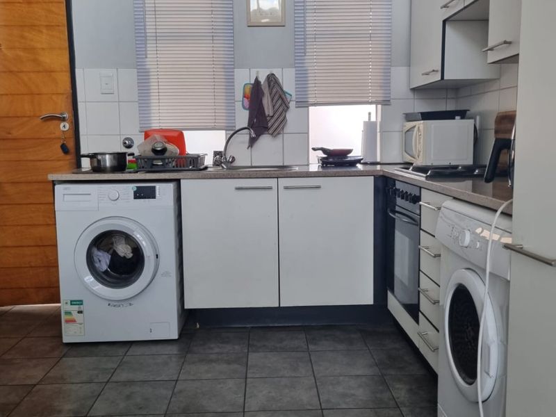 Functional kitchen featuring white cabinetry, tiled backsplash, built-in oven, and integrated laundry appliances with dark floor tiling.