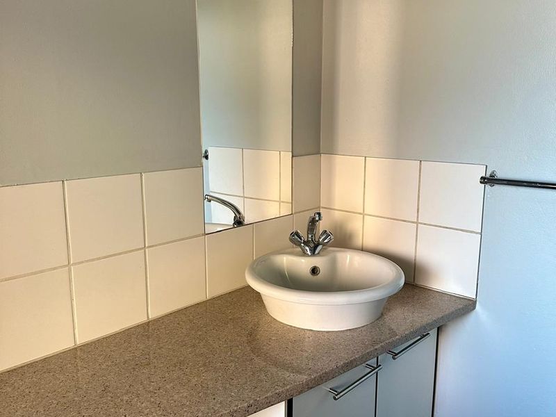 A clean bathroom vanity area featuring a modern vessel sink, stone-look countertop, wall-mounted cabinetry, and a tiled splashback.