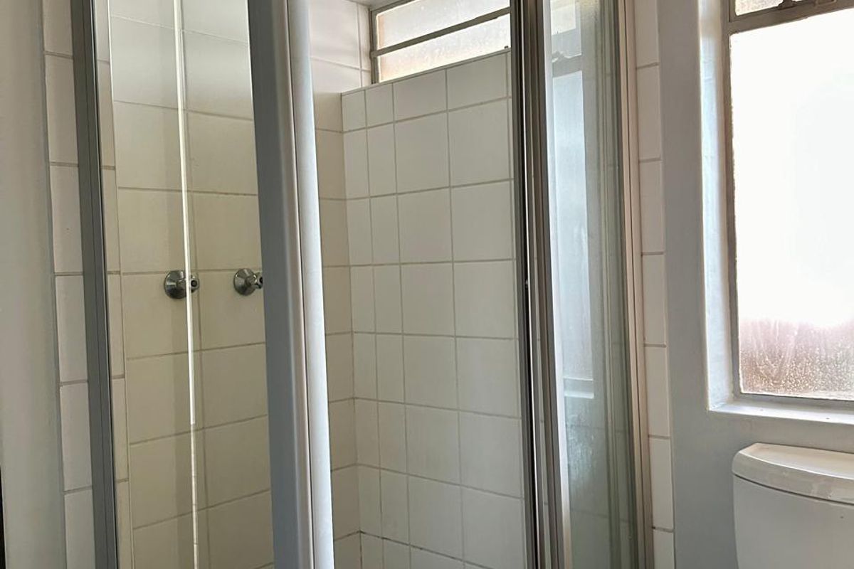 A functional bathroom featuring a glass-enclosed shower with tiled walls and a standard toilet, offering a clean, neutral space ready for updates.