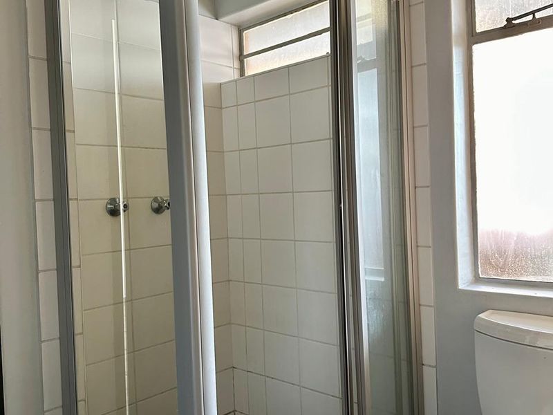 A functional bathroom featuring a glass-enclosed shower with tiled walls and a standard toilet, offering a clean, neutral space ready for updates.