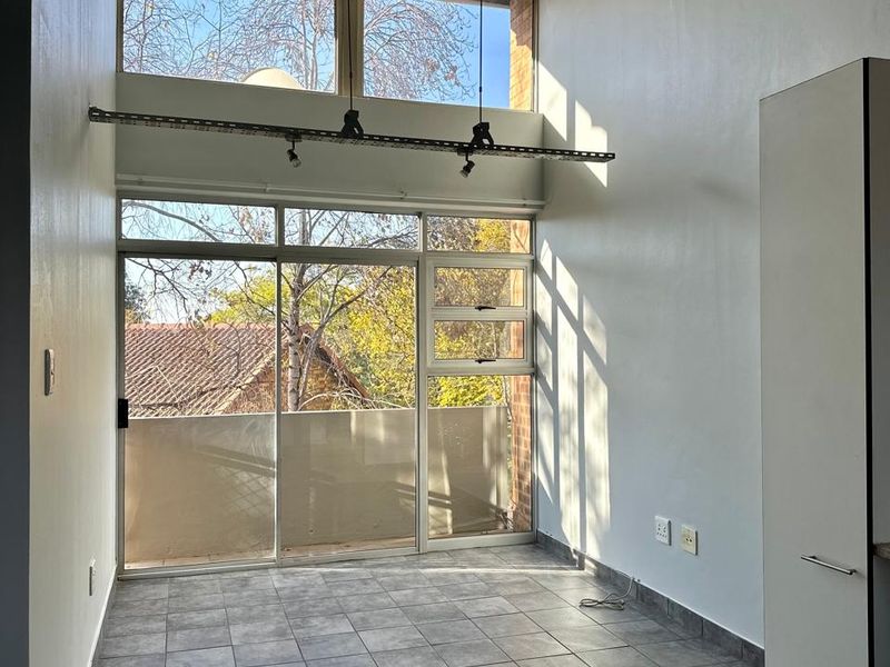 Bright open-plan living area featuring double-height ceilings, large sliding glass doors leading to a balcony, and modern tiled flooring.