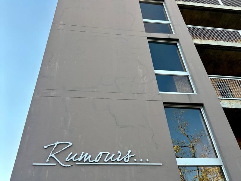 Low angle view of the apartment building facade featuring large windows, balcony railings, and exterior signage.
