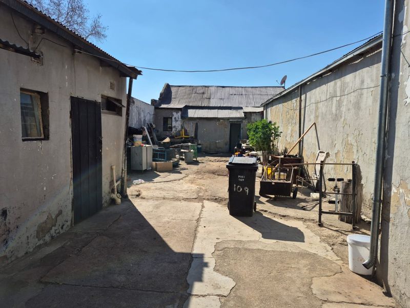 A rear exterior courtyard area featuring weathered plastered walls, corrugated metal roofing, and cracked concrete paving in need of maintenance.