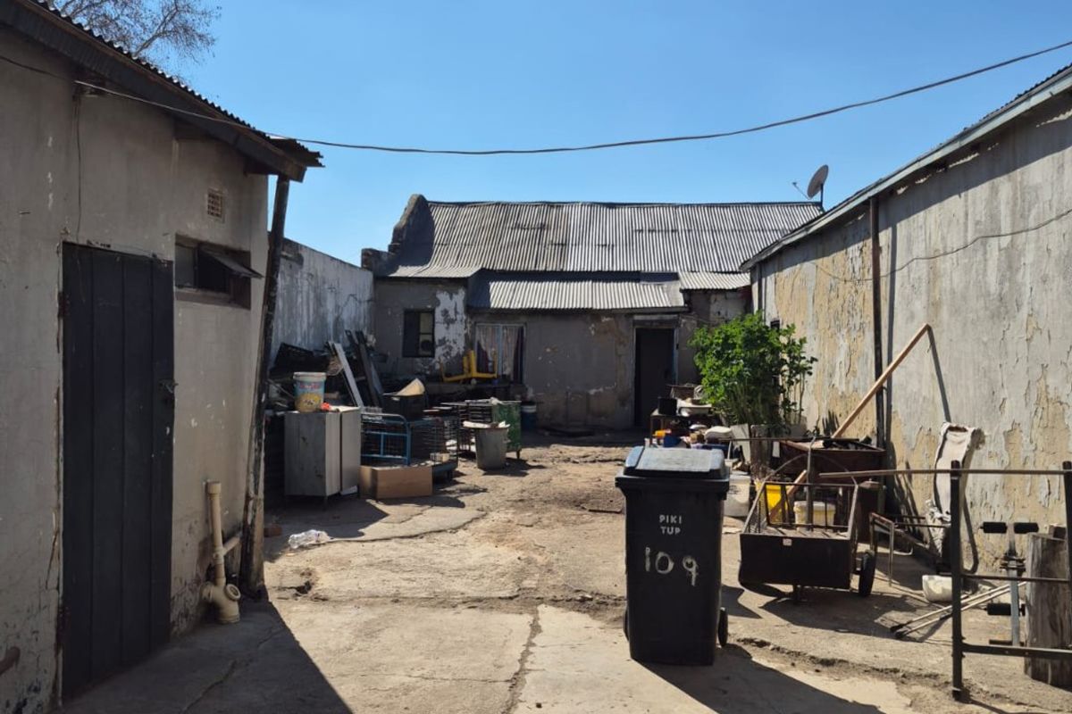 Rear exterior courtyard area featuring concrete paving and surrounding boundary walls with weathered finishes and corrugated metal roofing structures.