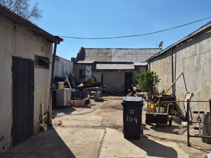 Rear exterior courtyard area featuring concrete paving and surrounding boundary walls with weathered finishes and corrugated metal roofing structures.