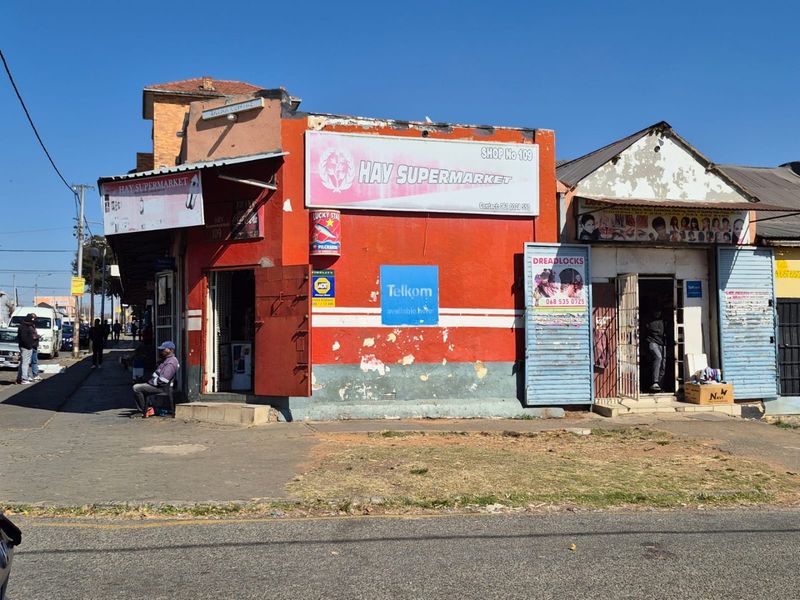 Street-level view of a commercial building featuring multiple shop fronts with security gates and signage in a high-traffic urban area.