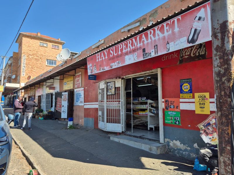 Street-level view of a commercial retail shopfront featuring prominent signage, security gates, and an awning along a public sidewalk.