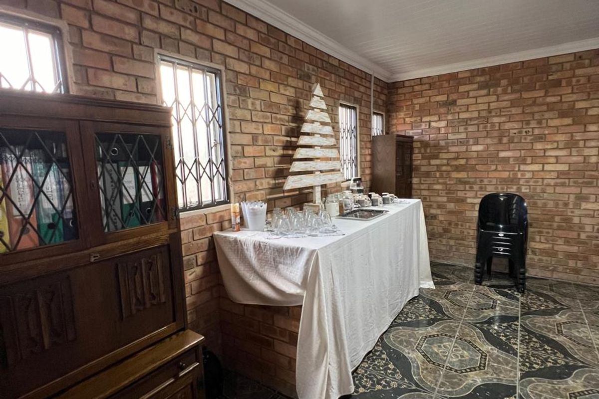 A multi-purpose room featuring exposed face-brick walls, patterned ceramic floor tiles, and security bars on the windows.