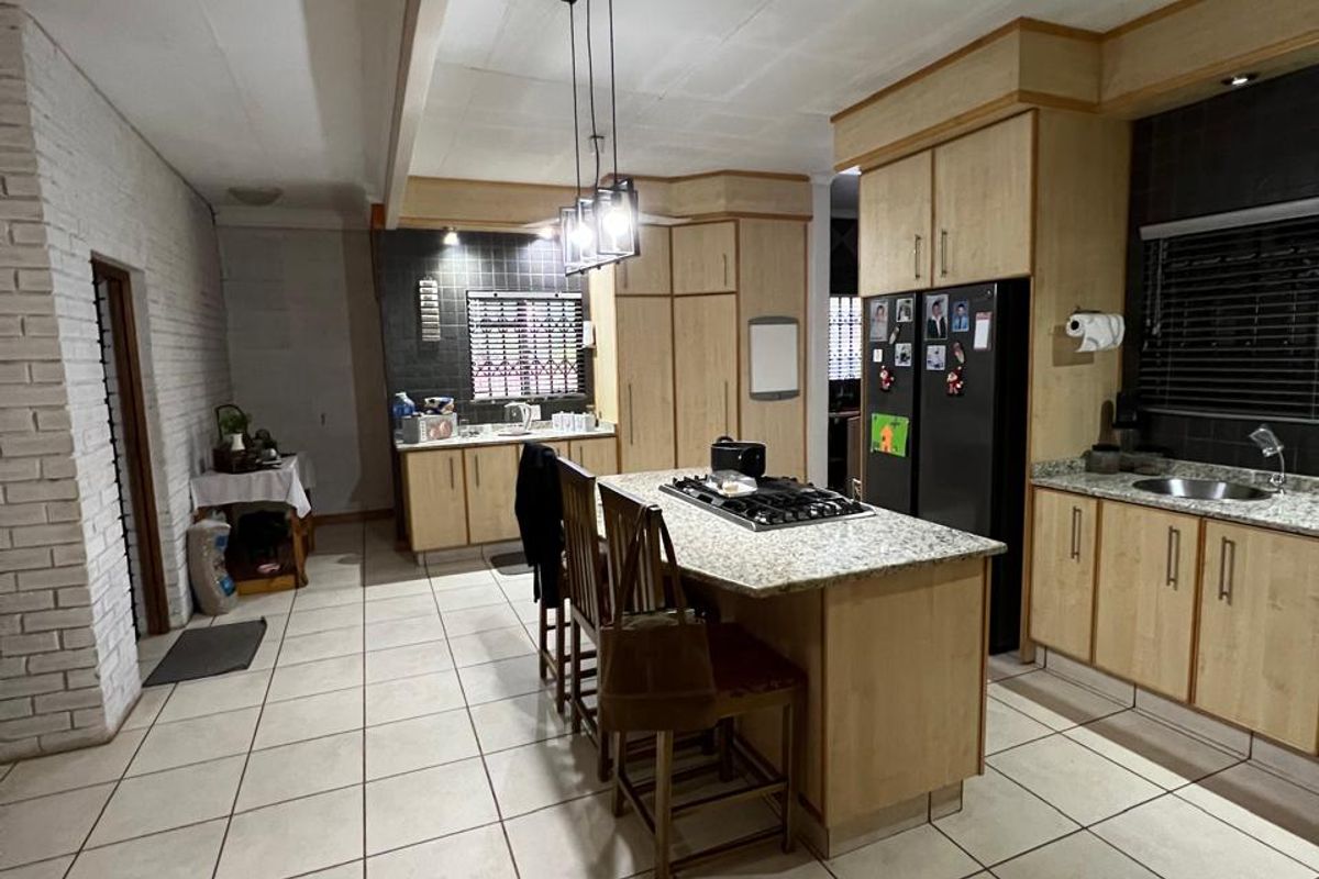 Spacious kitchen featuring light wood cabinetry, granite countertops, a central island with a built-in gas hob, and tiled flooring throughout.