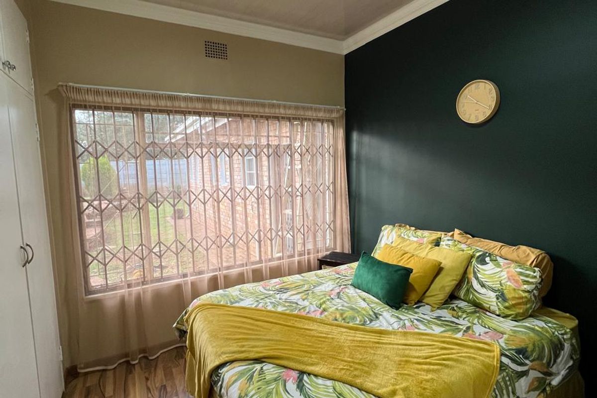 A bedroom featuring wood-look flooring, built-in cupboards, and a large window with security bars, finished with a dark accent wall.