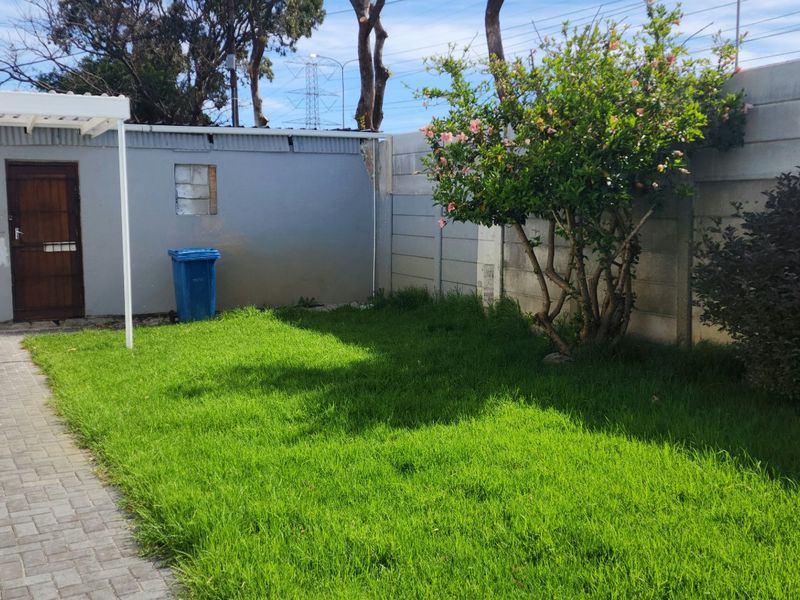 A private rear garden featuring a paved walkway, a small covered patio area, and a lawn enclosed by precast concrete boundary walls.