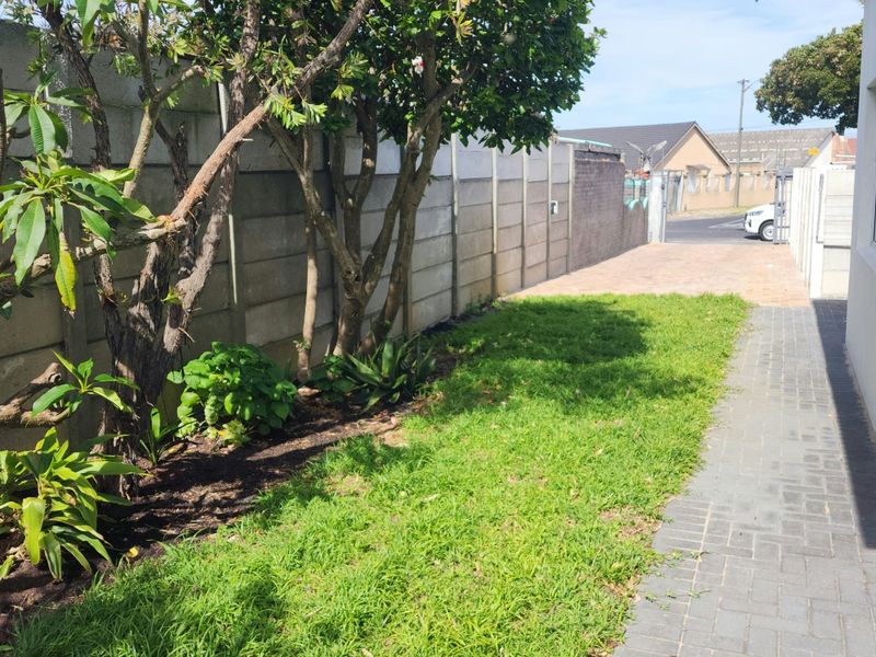 A side garden area featuring a paved walkway, lawn, and a precast concrete boundary wall, providing a clean and functional outdoor space.