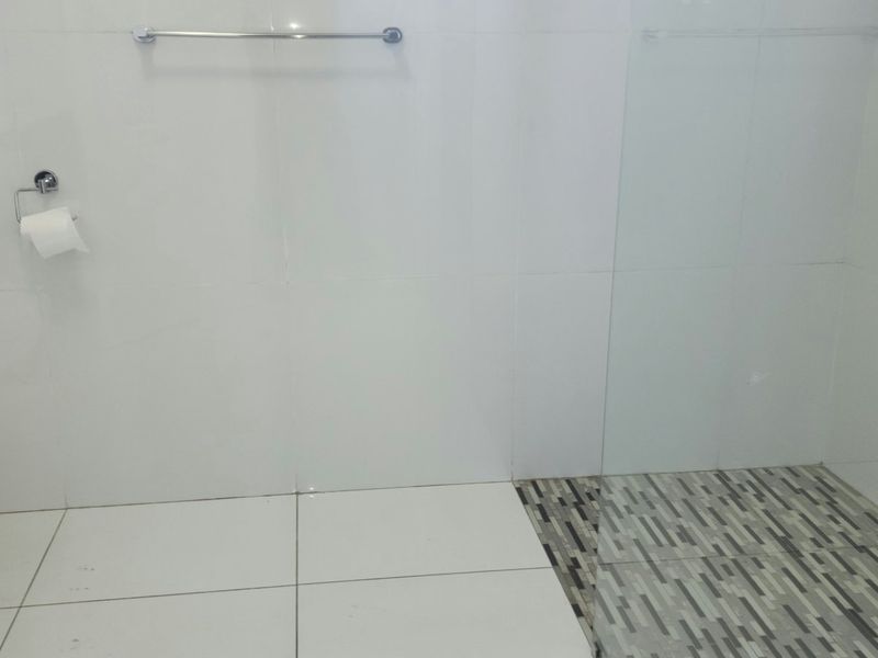 A clean, modern bathroom featuring a wall-mounted toilet, bidet spray, glass shower screen, and contrasting mosaic floor tiling.
