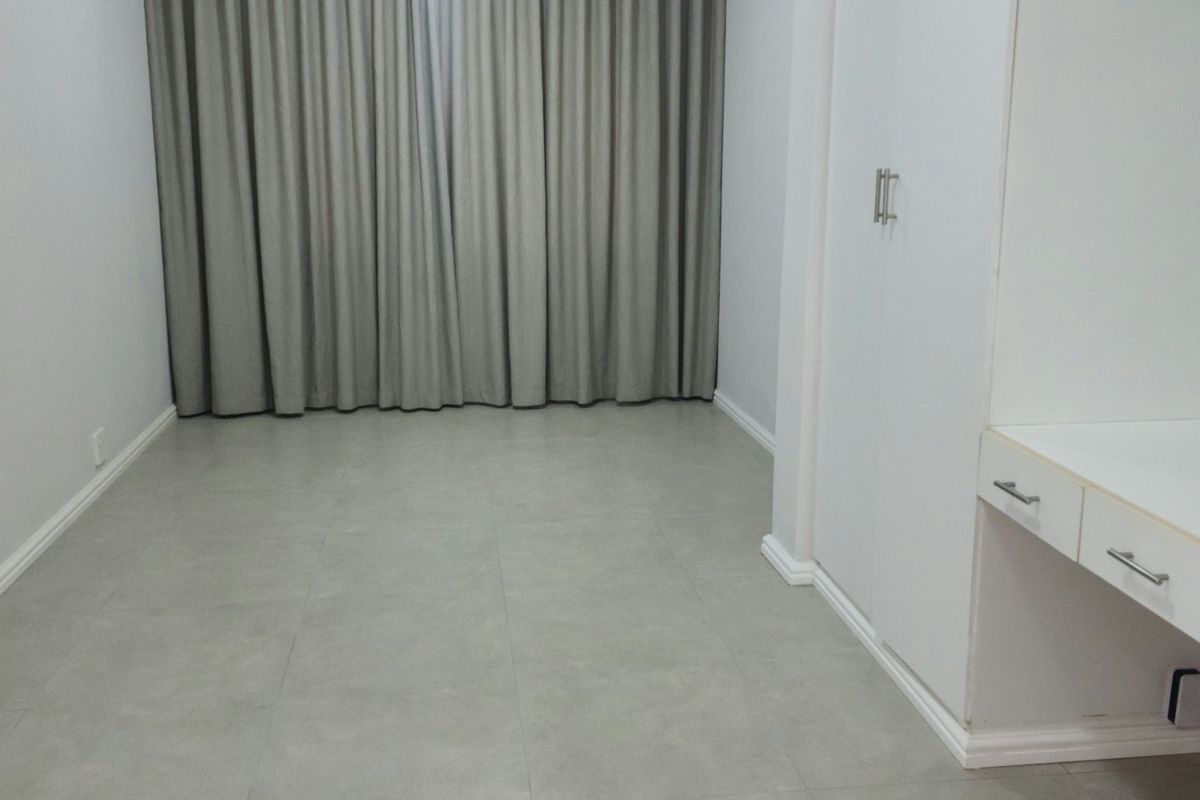 An empty bedroom featuring neutral tiled flooring, built-in wardrobe storage, and a built-in vanity unit with clean white finishes.