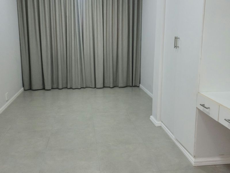 An empty bedroom featuring neutral tiled flooring, built-in wardrobe storage, and a built-in vanity unit with clean white finishes.