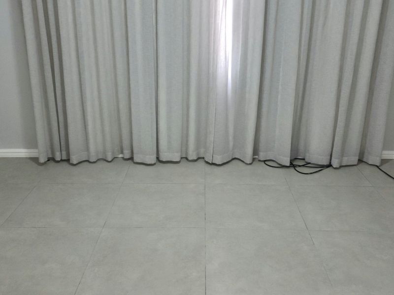 A clean, empty room featuring neutral grey tiled flooring, matching wall paint, and full-length curtains, providing a versatile space ready for furnishing.
