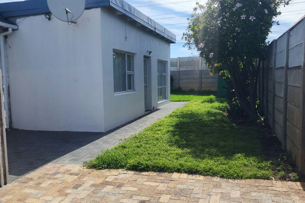 Rear exterior view of the property featuring a paved walkway, small lawn area, and precast concrete boundary walls.