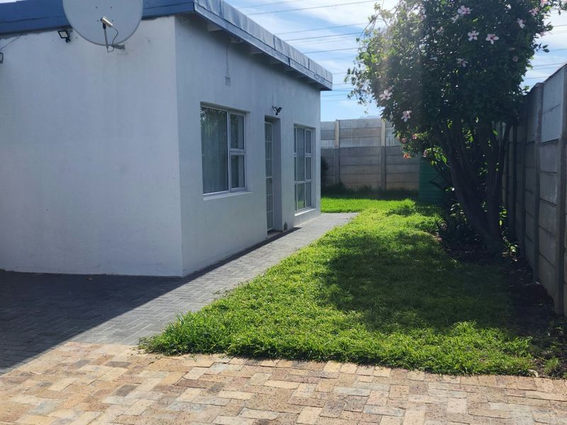 Rear exterior view of the property featuring a paved walkway, small lawn area, and precast concrete boundary walls.