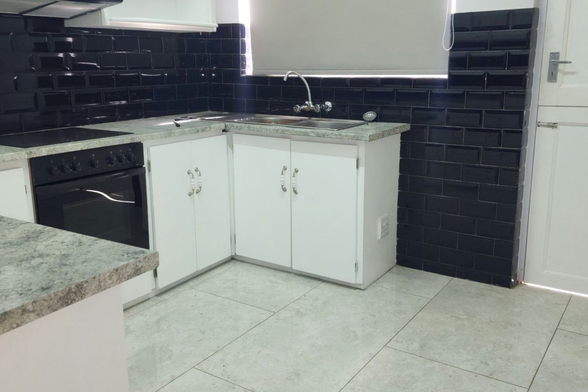 A clean, functional kitchen featuring white cabinetry, granite-look laminate countertops, black subway tile backsplash, and integrated oven and hob.