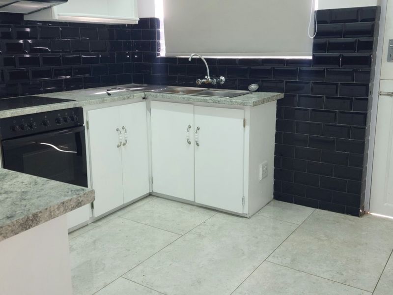 A clean, functional kitchen featuring white cabinetry, granite-look laminate countertops, black subway tile backsplash, and integrated oven and hob.