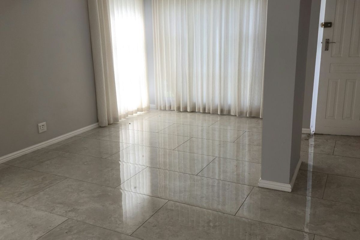 A bright, empty living area featuring modern large-format porcelain floor tiles, neutral grey walls, and a classic panel door.