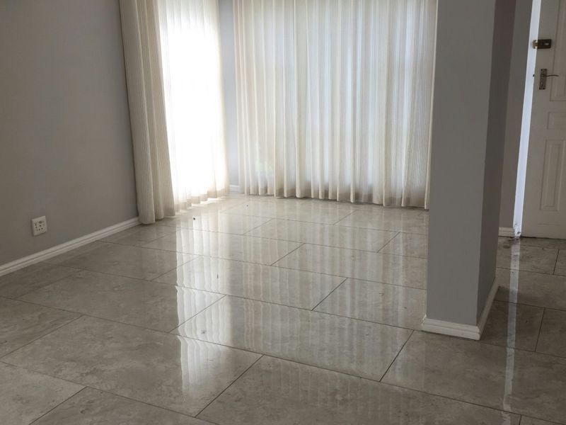 A bright, empty living area featuring modern large-format porcelain floor tiles, neutral grey walls, and a classic panel door.