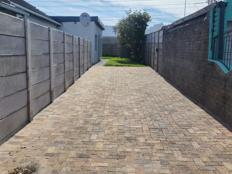 A paved driveway leading to the property, enclosed by precast concrete and brick boundary walls with installed electric fencing.