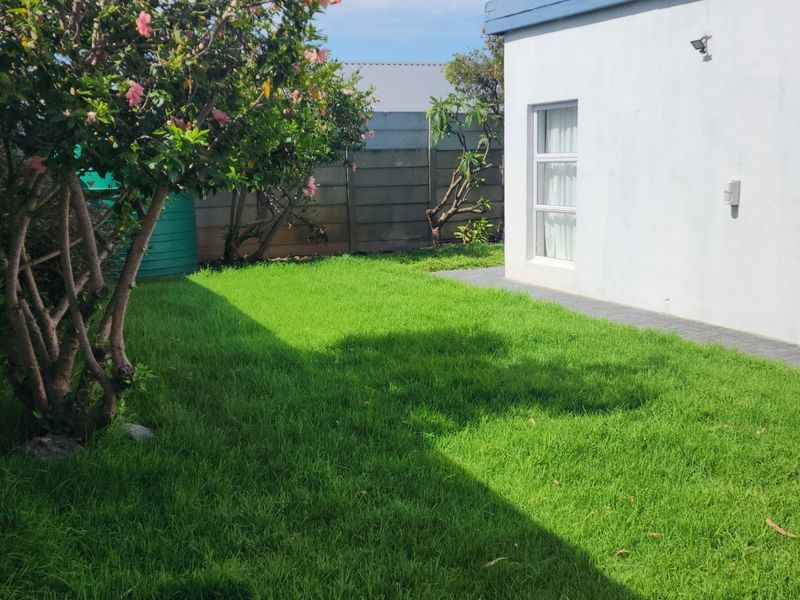 A private rear garden featuring a well-maintained lawn, paved walkway, and secure precast concrete boundary walls.