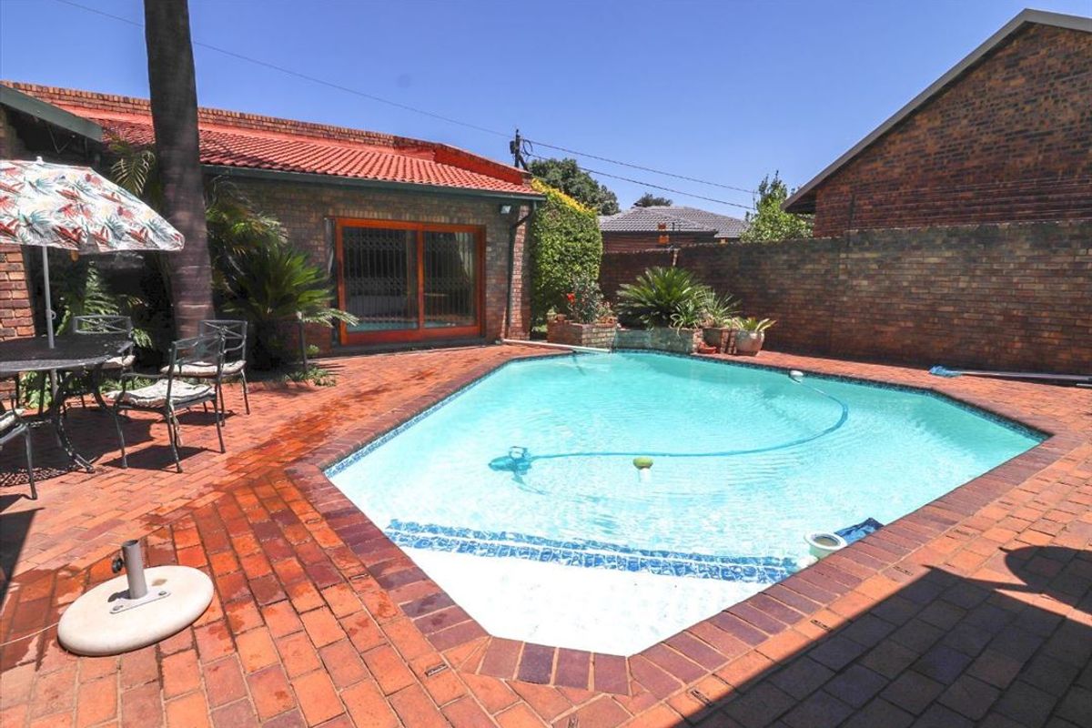 A private backyard featuring a swimming pool surrounded by brick paving, enclosed by a brick boundary wall, and adjacent to the main house structure.