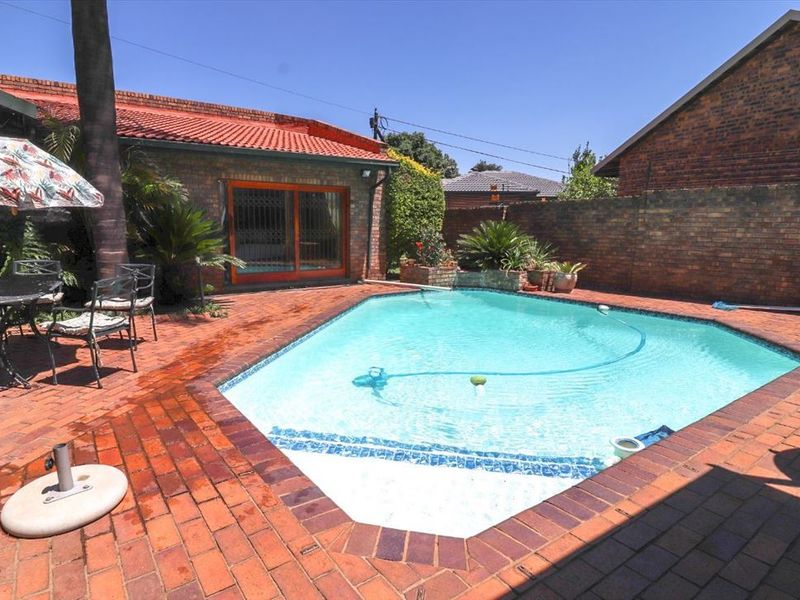 A private backyard featuring a swimming pool surrounded by brick paving, enclosed by a brick boundary wall, and adjacent to the main house structure.
