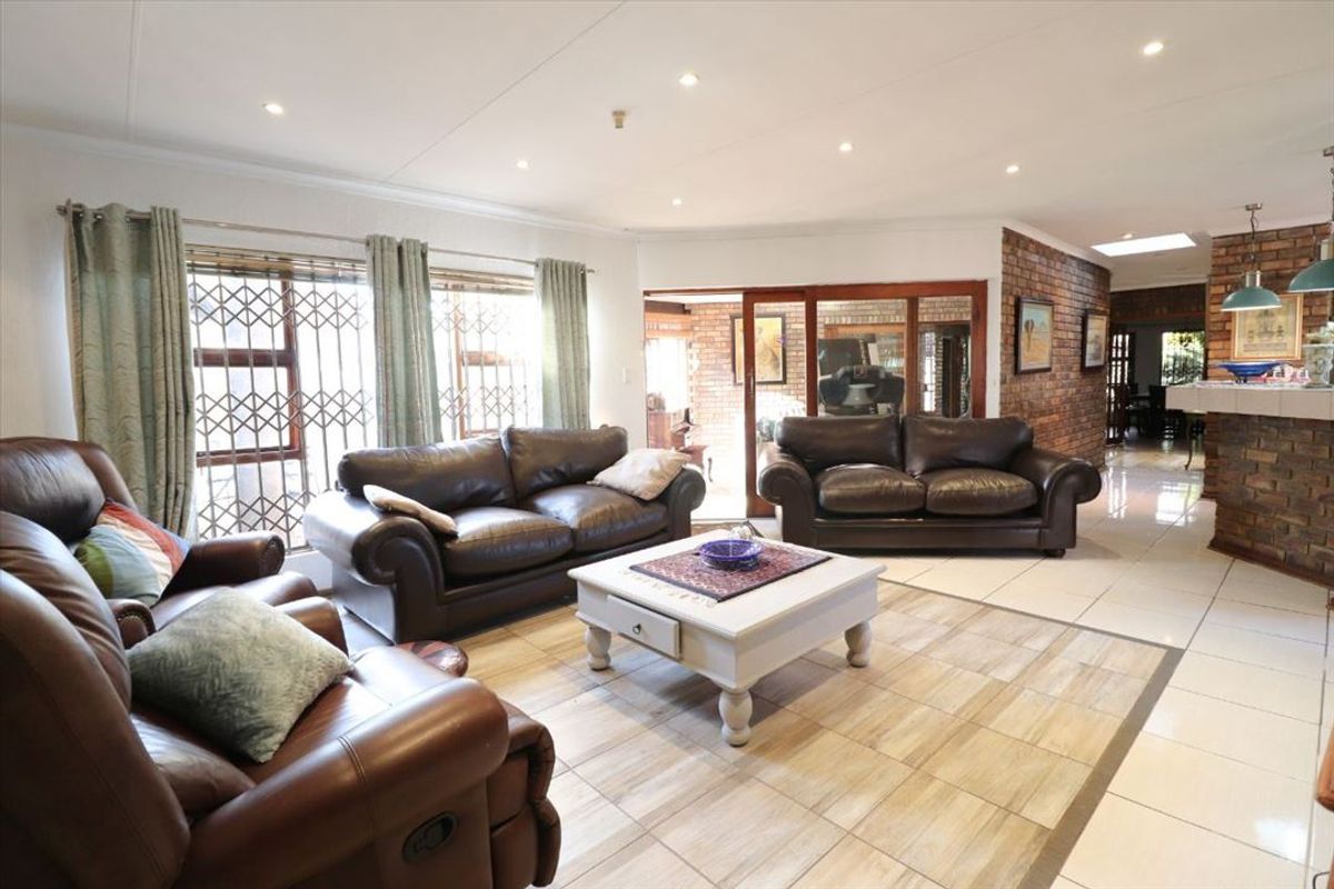 Spacious open-plan living area featuring tiled flooring, recessed ceiling lighting, and a feature brick wall, seamlessly connecting to the adjacent dining space.