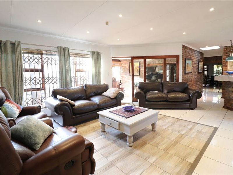Spacious open-plan living area featuring tiled flooring, recessed ceiling lighting, and a feature brick wall, seamlessly connecting to the adjacent dining space.