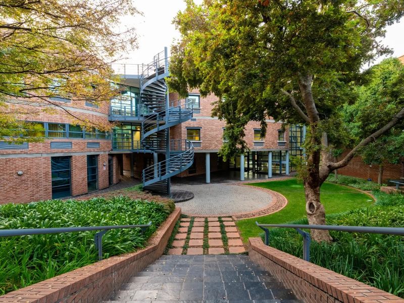 A well-maintained commercial courtyard featuring a distinctive spiral staircase, brick building facade, paved circular area, and landscaped garden surroundings.