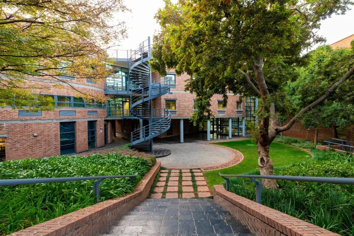 A well-maintained commercial courtyard featuring a distinctive spiral staircase, brick building facade, paved circular area, and landscaped garden surroundings.