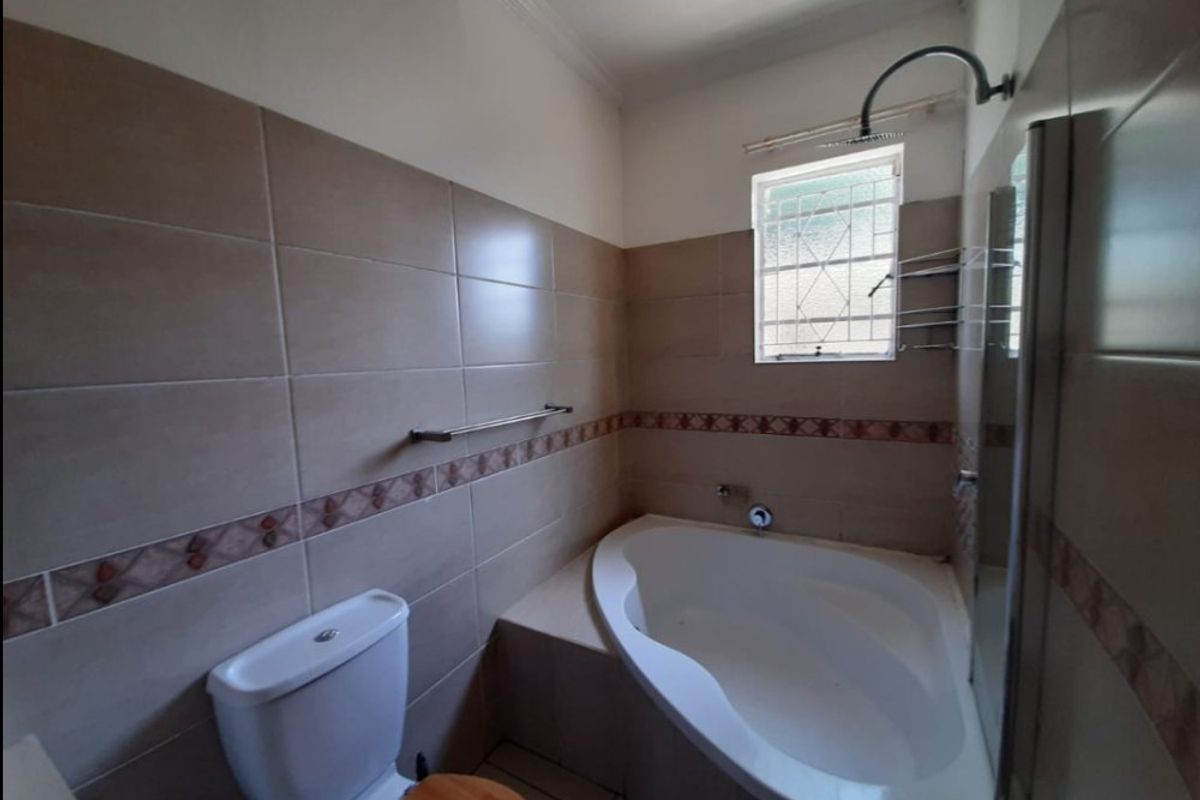 A functional bathroom featuring a built-in corner bathtub, shower fixture, and toilet with neutral wall tiling.
