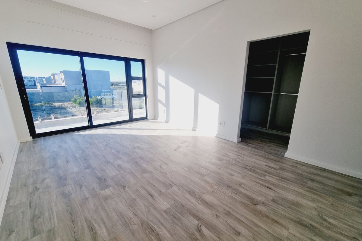 A bright, modern bedroom featuring light wood-look flooring, large sliding glass doors, and a built-in walk-in closet area.