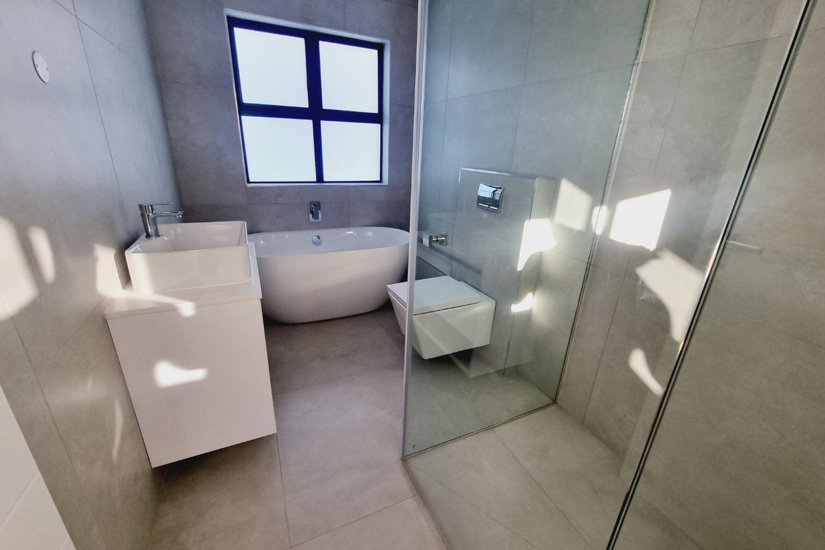 Modern bathroom featuring a freestanding bathtub, wall-mounted toilet, glass-enclosed shower, and a contemporary vanity unit with grey floor-to-ceiling tiling.
