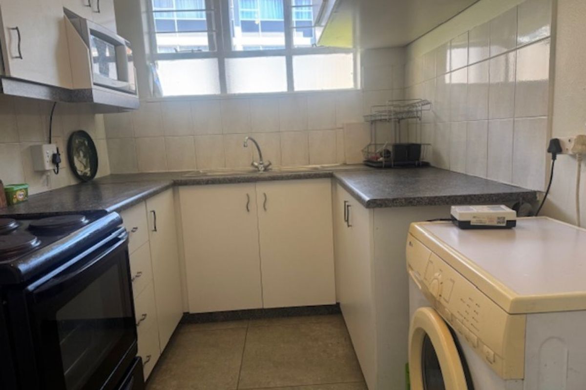 A functional kitchen featuring built-in cabinetry, laminate countertops, a stainless steel sink, and tiled backsplash, offering a practical layout for daily use.