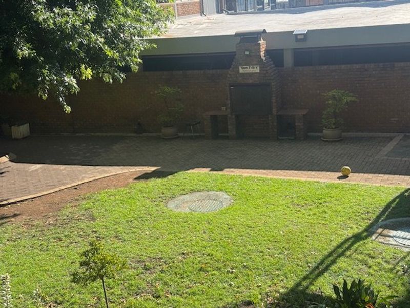 A private rear garden area featuring a paved patio, a built-in brick braai, and a well-maintained lawn enclosed by a brick boundary wall.