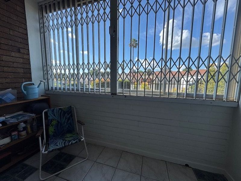 Enclosed balcony area featuring tiled flooring, brick wall accents, and security gates, offering a functional outdoor space with neighborhood views.