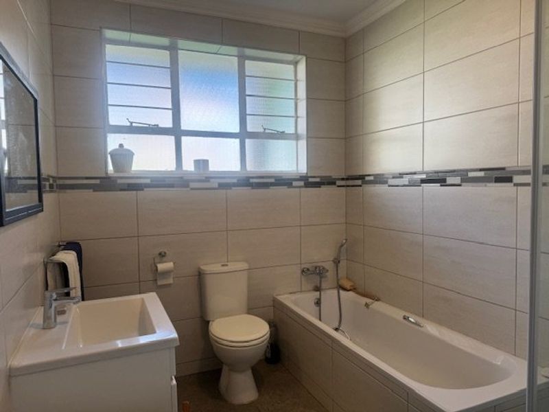 A well-maintained bathroom featuring a vanity basin, toilet, and bathtub with a handheld shower mixer, finished with modern wall tiling.